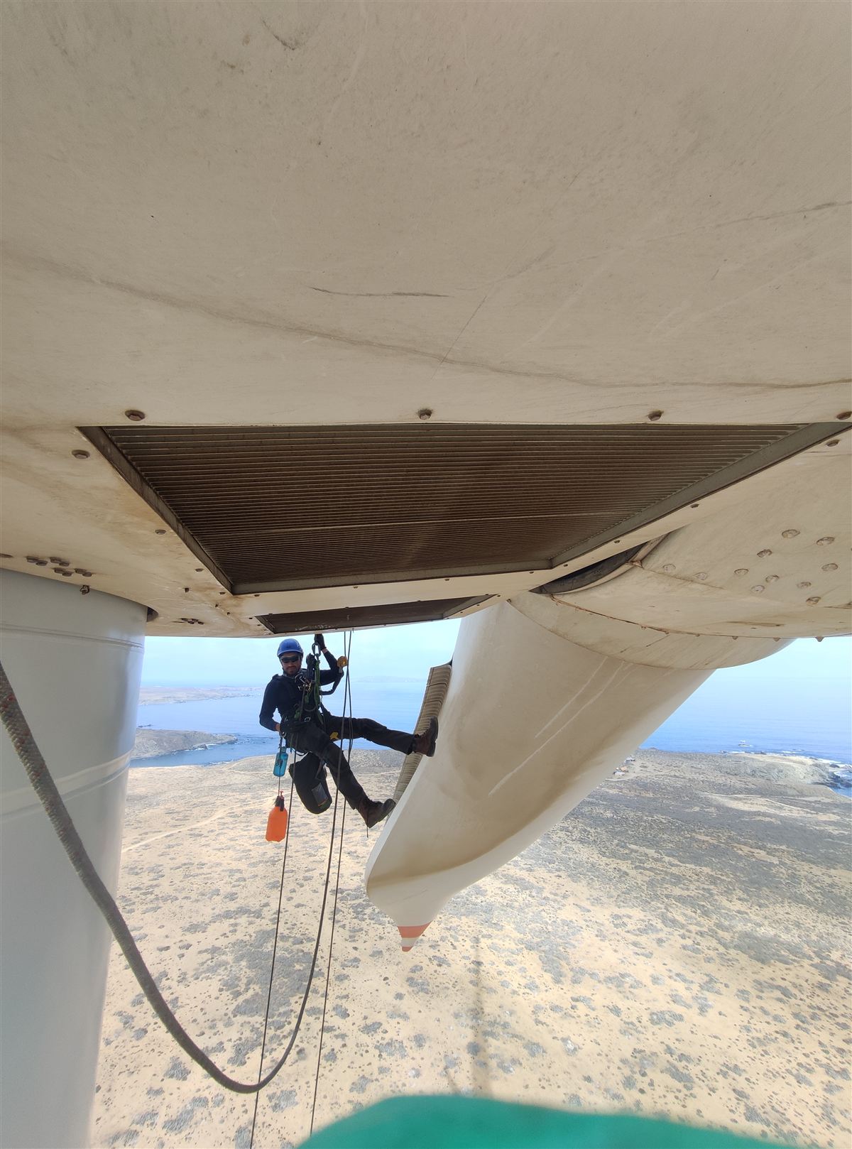 Técnico ANCORD suspendido en cuerda bajo una pala de aerogenerador, con arnés y equipo de seguridad